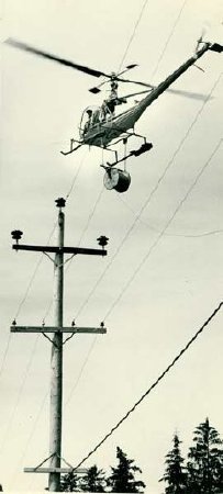 Helicopter on skids hauling cable between poles